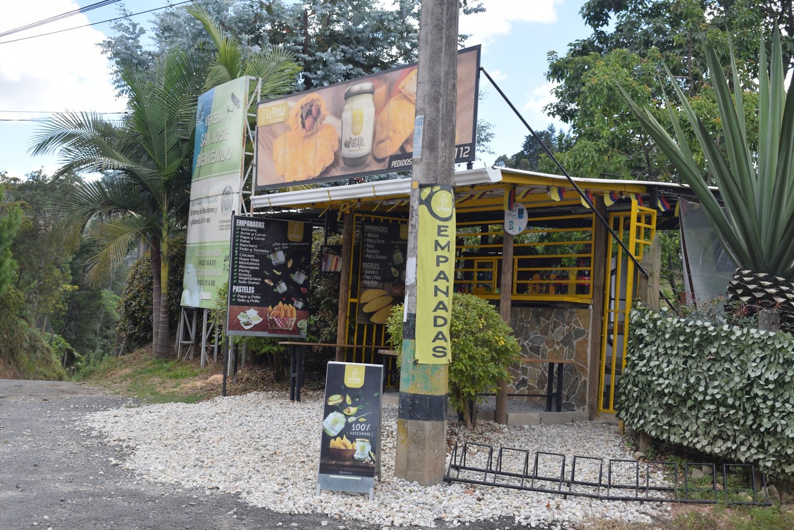 Fachada de La Piedad en el km 1 de la vía al aeropuerto JMC: caseta amarilla con la carta de empanadas y pasteles